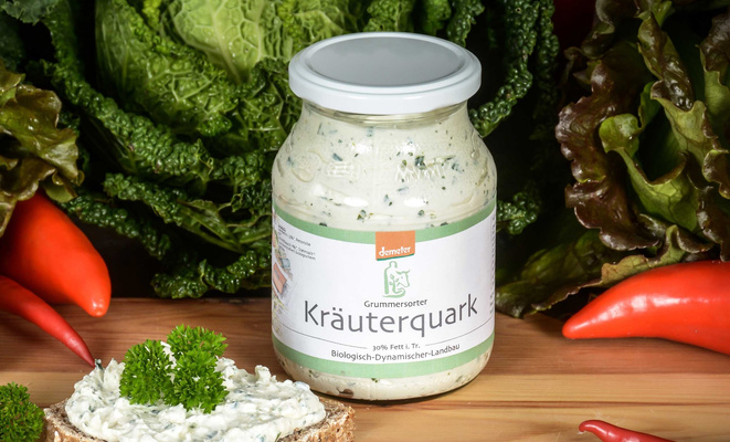 KI generiert: Ein Glas Kräuterquark von Demeter vor frischem Gemüse; Text: "Grummersorter Kräuterquark".