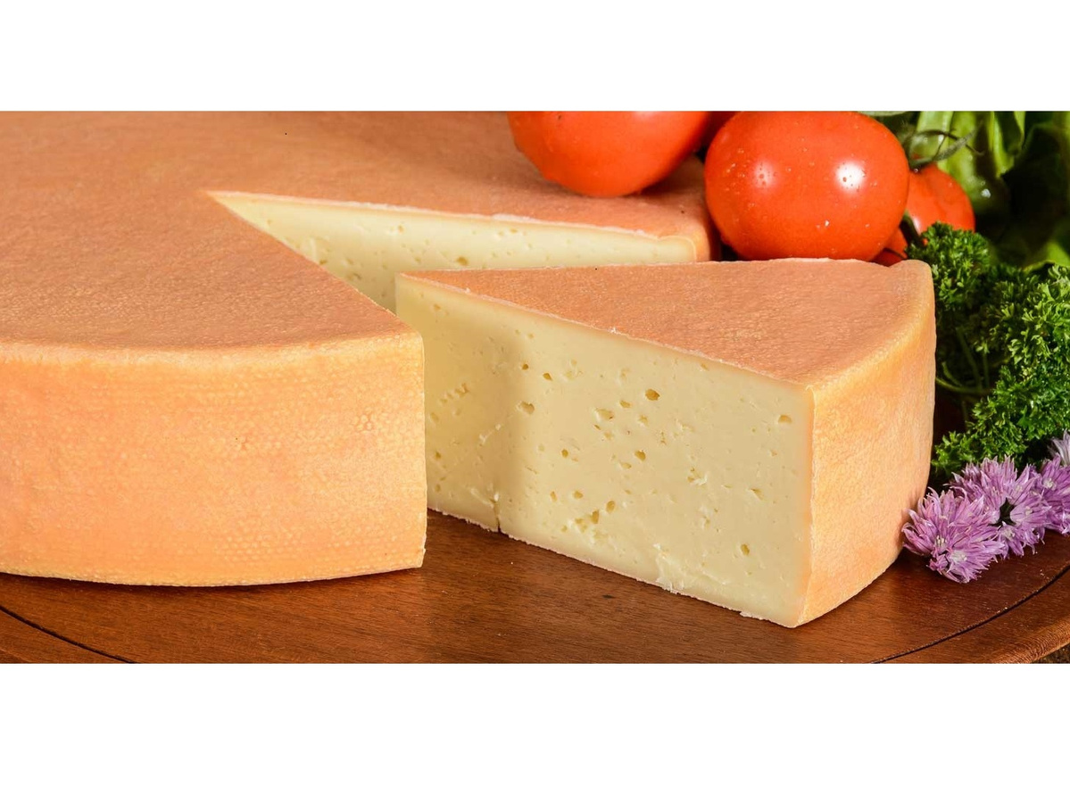 KI generiert: Ein runder Käse mit einem herausgeschnittenen Stück, dekoriert mit Tomaten und Kräutern.