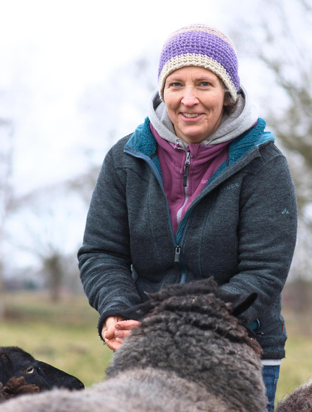 KI generiert: Eine Person mit Mütze strahlt in die Kamera und ist von Schafen umgeben.