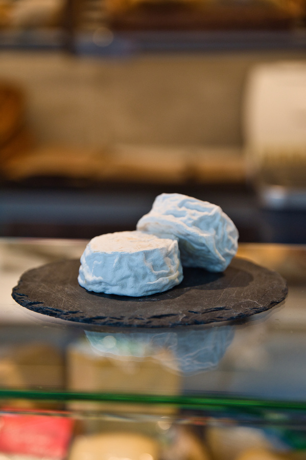 KI generiert: Zwei runde Käsestücke auf einer schwarzen Schieferplatte, unscharfer Hintergrund.